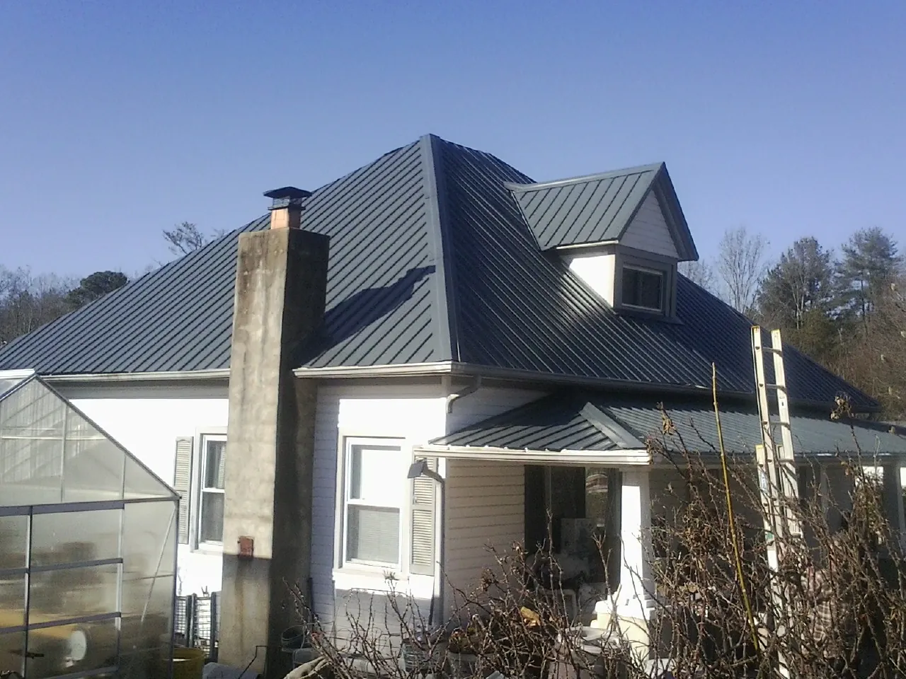 Dark blue standing seam metal roof on a white farmhouse with dormer — Slate & Tile Roof Repair by Roofing Brothers in Hurdle Mills
