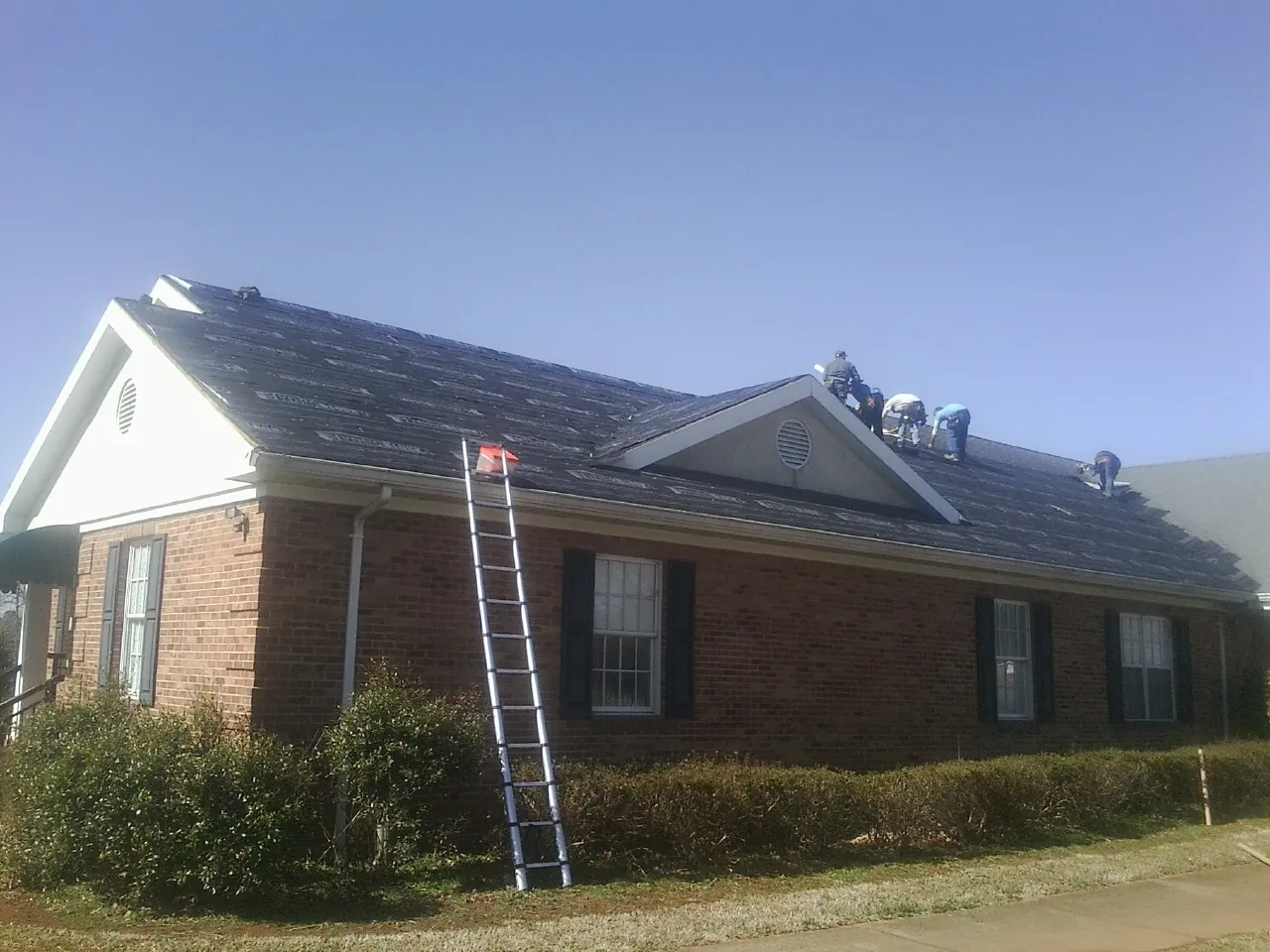 Crew tearing shingles off a brick ranch roof with a ladder set — Metal Roof Repair work by our crew in Hurdle Mills