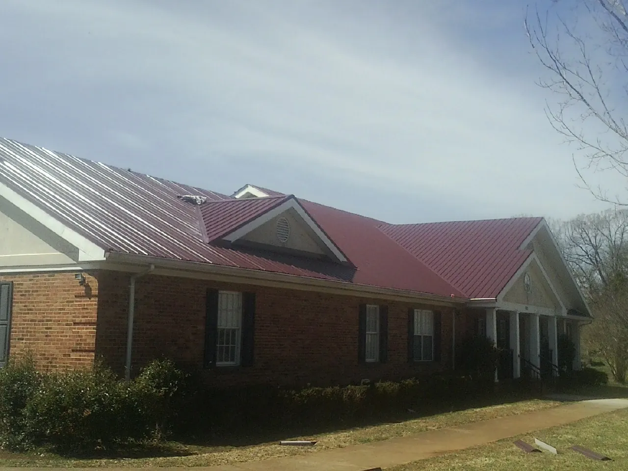 Red metal roof with gabled entries on a long brick building, from a Hail Damage Roof Repair job in Hurdle Mills
