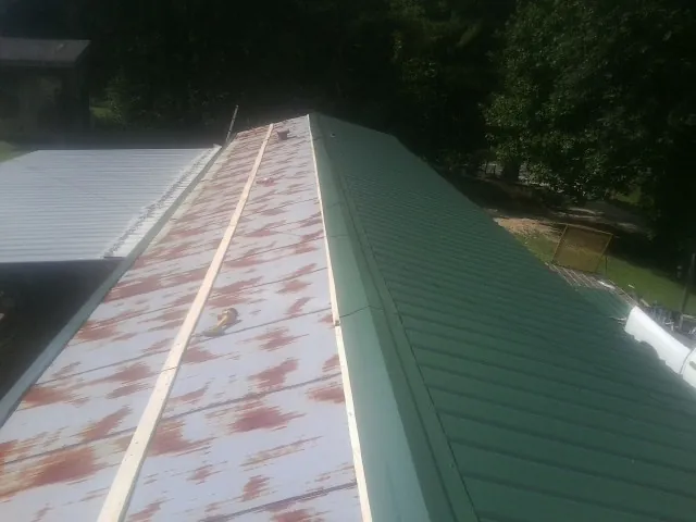 Old rusted panels beside newly installed green metal roofing — Wind Damage Roof Repair by Roofing Brothers in Hurdle Mills