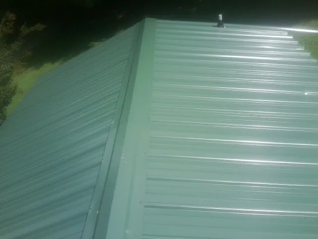 New green metal panels meeting at the ridge of a roof — Flat Roof Repair work by our crew in Hurdle Mills