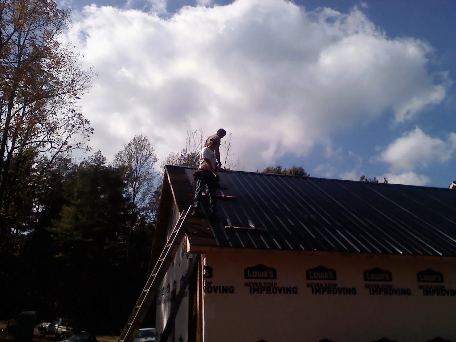 Roofer fastening dark metal panels high against a cloudy sky in Hurdle Mills