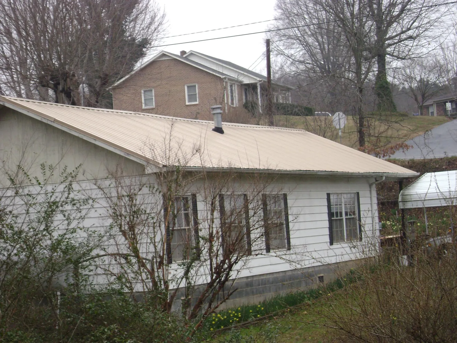 Tan metal roof on a white sided house set into a hillside — Commercial Roofing by Roofing Brothers in Hurdle Mills