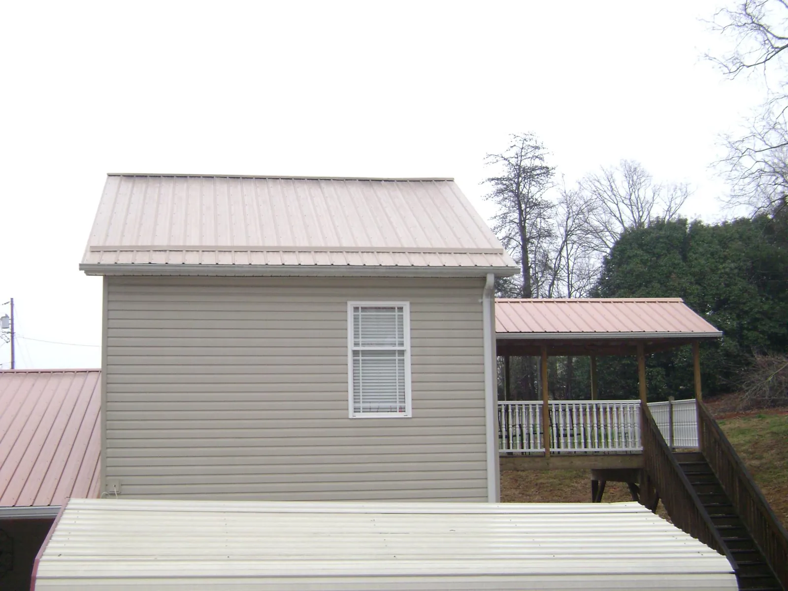 Tan metal roofs on a two story addition and attached porch, from a Roof Replacement job in Hurdle Mills